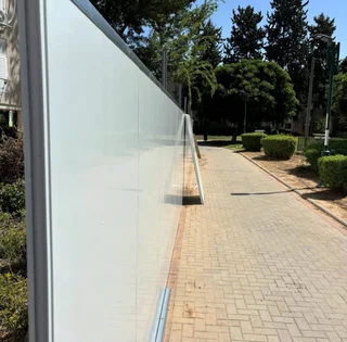 גדר פאנל בהירה וארוכה המפרידה שביל הולכי רגל מרוצף